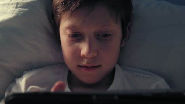 Jongen rusten in zijn bed in de avond met zijn digitale tablet — Stockvideo