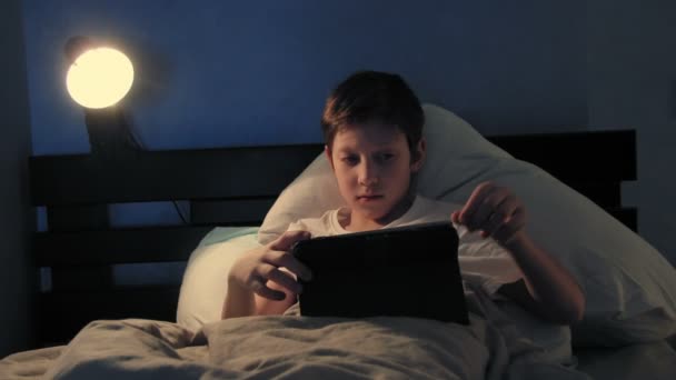 Мальчик отдыхает в своей постели по вечерам, используя свой цифровой планшет, выключая свет и засыпая — стоковое видео