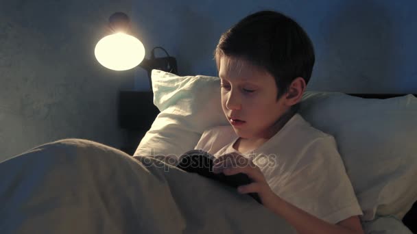 Αγόρι ανάπαυση στο κρεβάτι του το βράδυ και διαβάζοντας ένα βιβλίο — Αρχείο Βίντεο