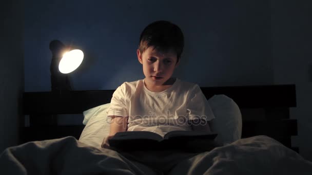 Jongen rusten in zijn bed in de avond en het lezen van een boek licht uitgeschakeld en gaat slapen — Stockvideo