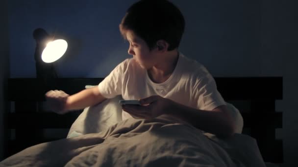 Garçon se reposant dans son lit le soir et en utilisant son téléphone intelligent et s'endort — Video