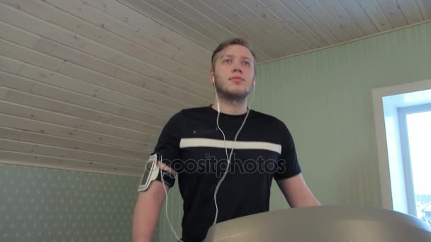Jonge man lopen op een loopband en luisteren naar muziek — Stockvideo