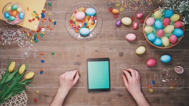 Hombre usando tableta digital en la mesa decorada con huevos de Pascua. Vista superior — Vídeos de Stock