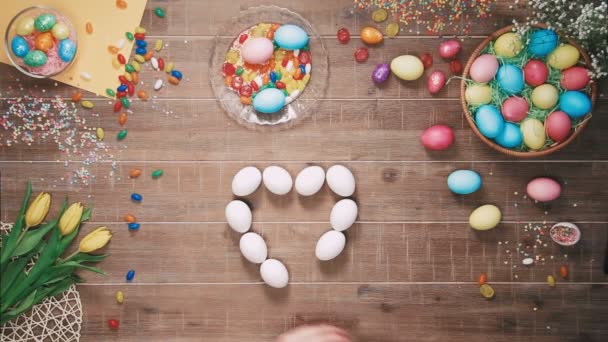 Hombre haciendo forma de corazón con huevos de Pascua en la mesa decorada con huevos de Pascua. Vista superior — Vídeos de Stock