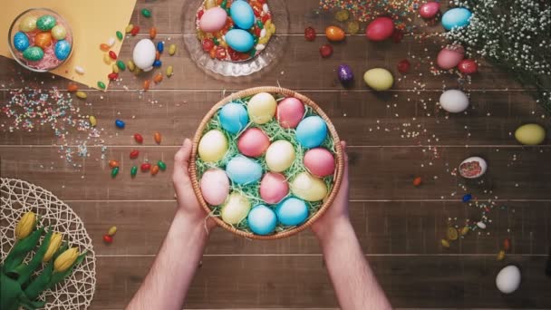 Hombre sosteniendo una cesta con huevos de Pascua en frente de la mesa decorada con huevos de Pascua. Vista superior — Vídeos de Stock