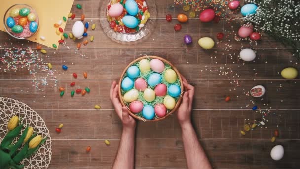 Cesta giratoria hombre con huevos de Pascua en la mesa decorada con huevos de Pascua. Vista superior — Vídeos de Stock