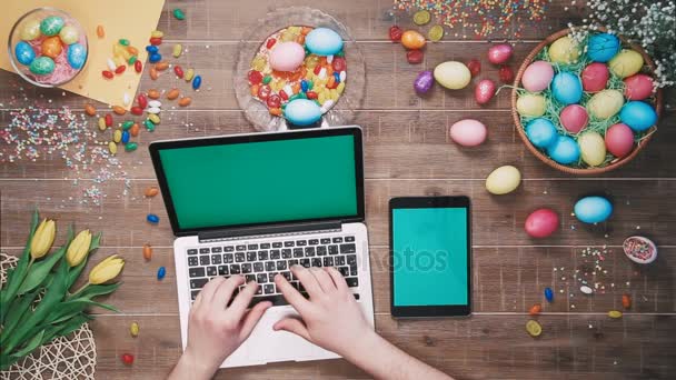 Uomo con computer portatile e tablet digitale con schermo verde sul tavolo decorato con uova di Pasqua Vista dall'alto — Video Stock