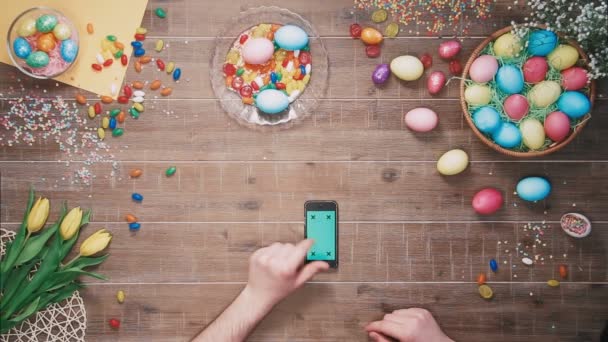 부활절 달걀 장식 테이블에 녹색 화면으로 스마트폰 사용 하는 사람. 상위 뷰 — 비디오