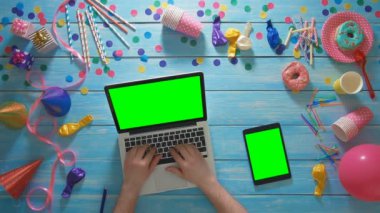 Üstten Görünüm adam dizüstü bilgisayar ve dijital tablet yeşil ekran kullanarak doğum günü partisi planlama