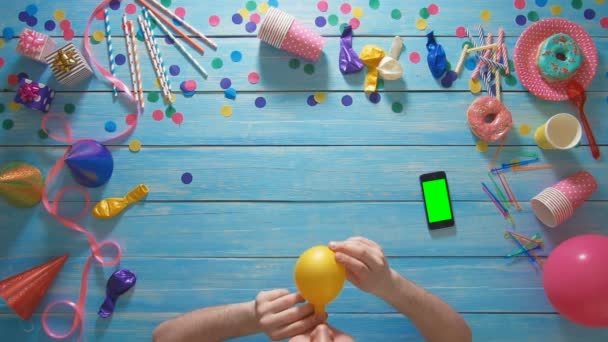 Top view hombre infla globo de cumpleaños, teléfono inteligente con pantalla verde en la mesa — Vídeos de Stock