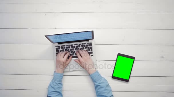 Vista superior manos masculinas que trabajan en el ordenador portátil y la tableta digital con pantalla verde que miente en el escritorio blanco desde arriba — Vídeo de stock