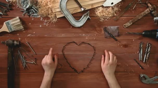 Верхний вид с задержкой руки, лежащей на деревянном столе формы сердца с винтами — стоковое видео