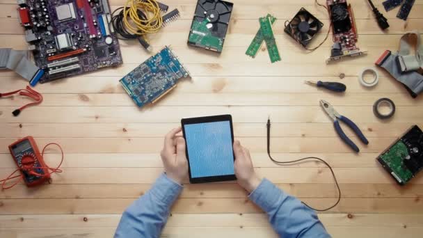 Top view computer technician using digital tablet with circuit board outline at wooden desk with tools and electronic components — Stock Video