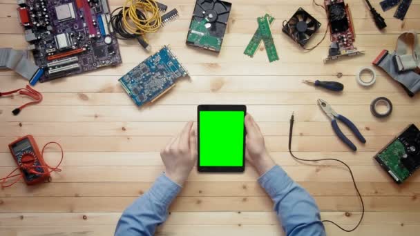 Técnico informático de vista superior que utiliza tableta digital con pantalla verde en escritorio de madera con herramientas y componentes electrónicos — Vídeo de stock