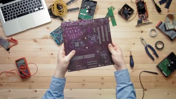 Top view computer technician holding computer motherboard at wooden desk with tools and electronic components — Stock Video