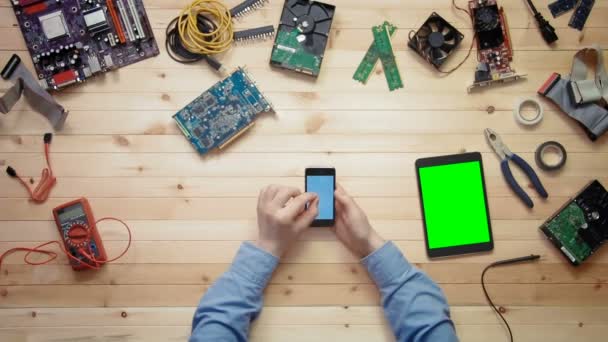 Üstten Görünüm bilgisayar teknisyen yeşil ekran araçları ve elektronik bileşenler ile ahşap masa başında yalan devre kartı anahat ve dijital tablet ile akıllı telefon kullanma — Stok video
