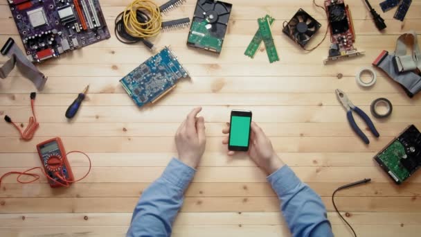 Ovanifrån datatekniker med smart telefon med grön skärm på trä skrivbord med verktyg och elektroniska komponenter — Stockvideo