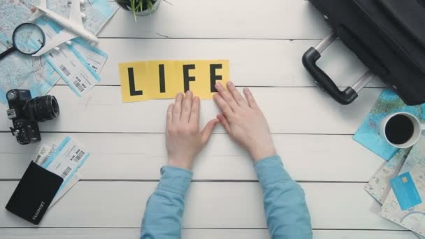 Vue du dessus time lapse mains posées sur un bureau blanc mot "LA VIE EST UN VOYAGE" décoré d'objets de voyage — Video