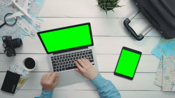 Bovenaanzicht reizigers handen met laptop en digitale tablet met groen scherm op witte houten bureau — Stockvideo