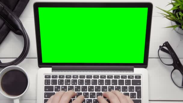 Männliche Hände arbeiten am Laptop mit grünem Bildschirm am weißen Schreibtisch von oben — Stockvideo