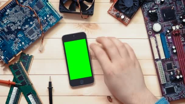 Top view computer technician showing multiple gestures on smart phone with green screen at wooden desk with tools and electronic components — Stock Video