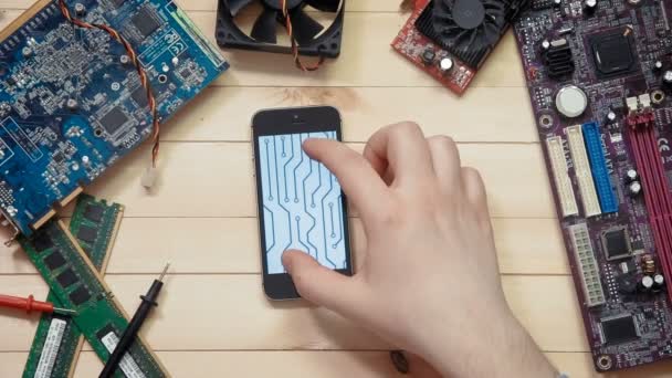 Pohled shora počítačový technik pomocí smartphone s obrysem obvodové desky na dřevěné desce s nástroji a elektronických součástek — Stock video