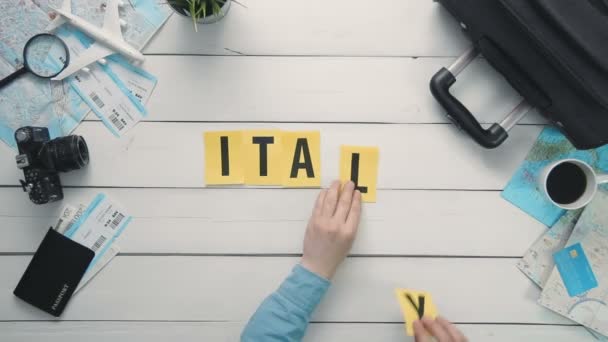 Vista superior lapso de tiempo manos que ponen en blanco palabra de escritorio "ITALIA" decorado con artículos de viaje — Vídeo de stock