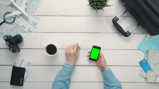 Bovenaanzicht reizigers hands aanduiding meerdere gebaren smartphone met groen scherm op witte houten bureau — Stockvideo