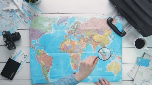 Pohled shora cestující ruce při pohledu na mapu světa pomocí zvětšovací sklo v bílé dřevěné stolní
