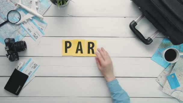 Вид зверху проміжок часу руки покласти на білий стіл слово "PARIS", прикрашений предметами подорожі — стокове відео