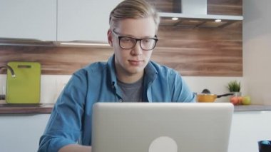 Genç adam evde dizüstü bilgisayar kullanıyor.