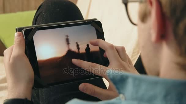 Młody człowiek ogląda obrazki w sieci społecznych za pomocą jego cyfrowego tabletu, szukam inspiracji — Wideo stockowe