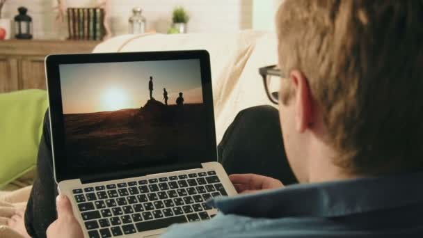Молодий чоловік дивиться фотографії в соціальній мережі за допомогою комп'ютера для ноутбуків, який шукає натхнення — стокове відео