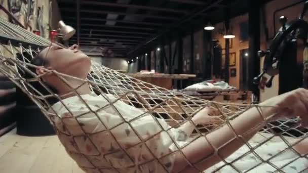Mulher com cabelo curto vestindo óculos relaxando na rede em seu apartamento loft — Vídeo de Stock