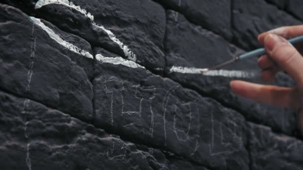Achteraanzicht close-up van jonge vrouwelijke schilder wit ontwerp maken op de zwarte bakstenen muur in de coffeeshop — Stockvideo