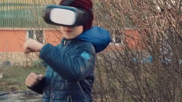 Маленький мальчик бледнеет файтинг с помощью гарнитуры виртуальной реальности на заднем дворе — стоковое видео