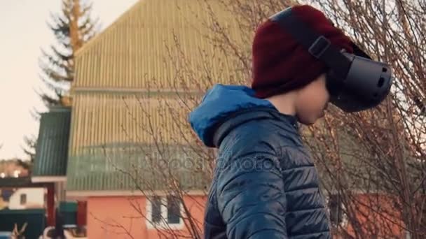 Μικρό αγόρι ψάχνει γύρω φορώντας σετ κεφαλής εικονικής πραγματικότητας στο κατώφλι — Αρχείο Βίντεο