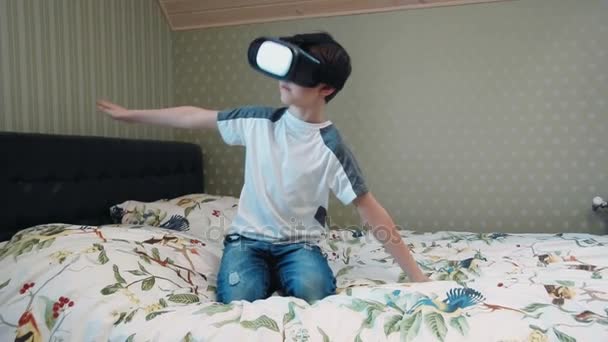 Μικρό αγόρι χρησιμοποιώντας σετ κεφαλής εικονικής πραγματικότητας με τον προσομοιωτή πτήσης που κάθεται στο κρεβάτι — Αρχείο Βίντεο