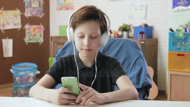Ładny mały chłopiec, słuchanie muzyki na jego smartphone noszenie słuchawek — Wideo stockowe