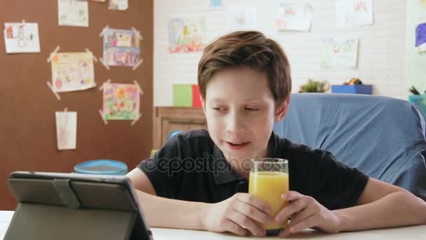 Schattige kleine jongen drinken oranje sap en wathcing grappige video 's — Stockvideo