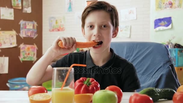 Lindo niño comiendo zanahoria y mirando a la cámara — Vídeo de stock