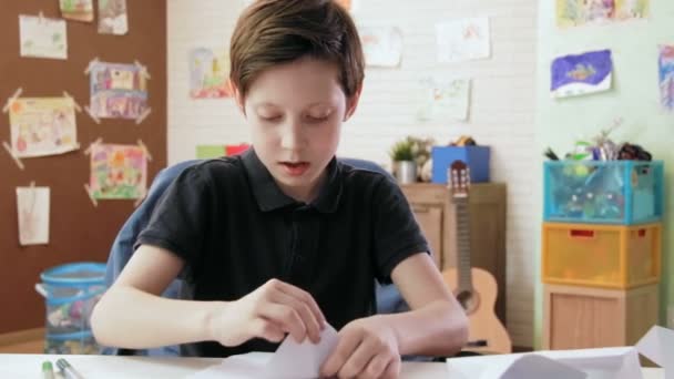 Милый мальчик складывает оригами в своей комнате — стоковое видео