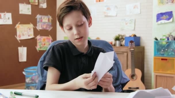 Leuke jongen origami vliegtuig vouwen in zijn kamer — Stockvideo