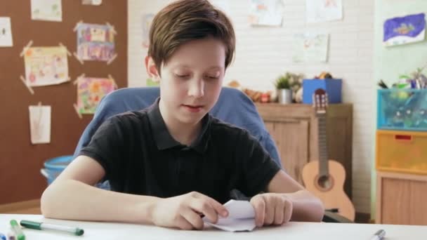 Cute boy folds origami boat and plays with it — Stock Video