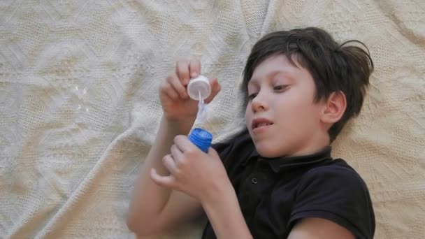 Bovenaanzicht van een schattige kleine jongen blazen van zeepbellen opleggen van het tapijt — Stockvideo