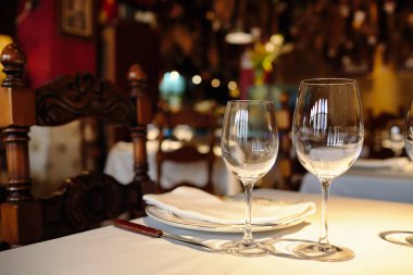 Beyaz masa örtüsü üzerinde bir restoranda boş gözlük. Gölge, kahverengi zemin ve oymalı sandalye.