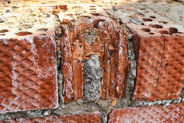 The old crumbling brick wall. Bricks and stones in the old wall. The old brick wall is falling apart. Close-up.