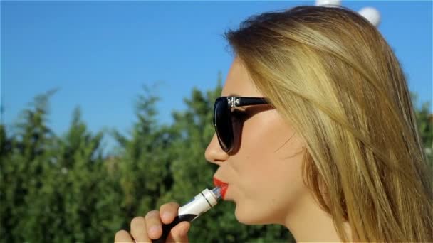 Молодая красивая девушка курит электронную сигарету — стоковое видео