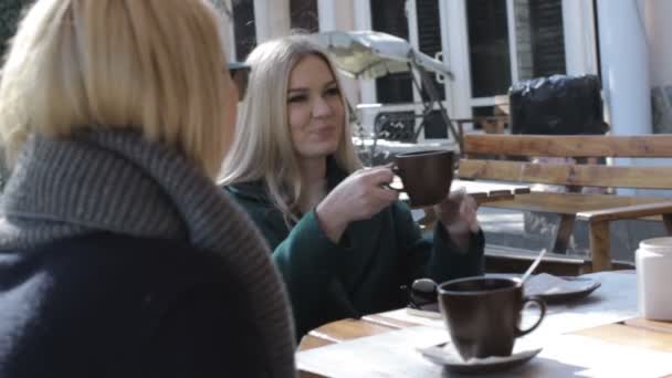 Two attractive young girls sit at an outdoor cafe and talk — Stock Video