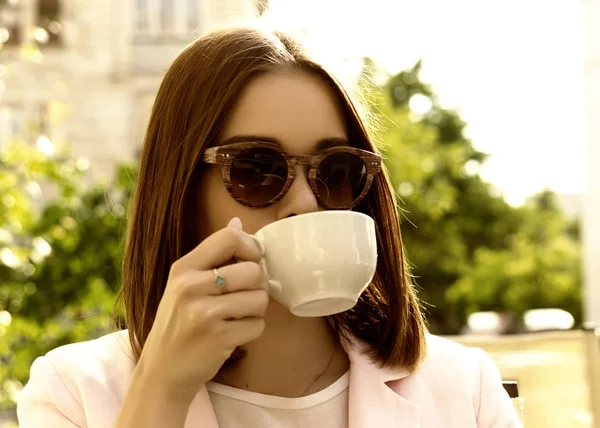 Jeune jolie fille boit une tasse de boisson chaude, en plein air — Photo